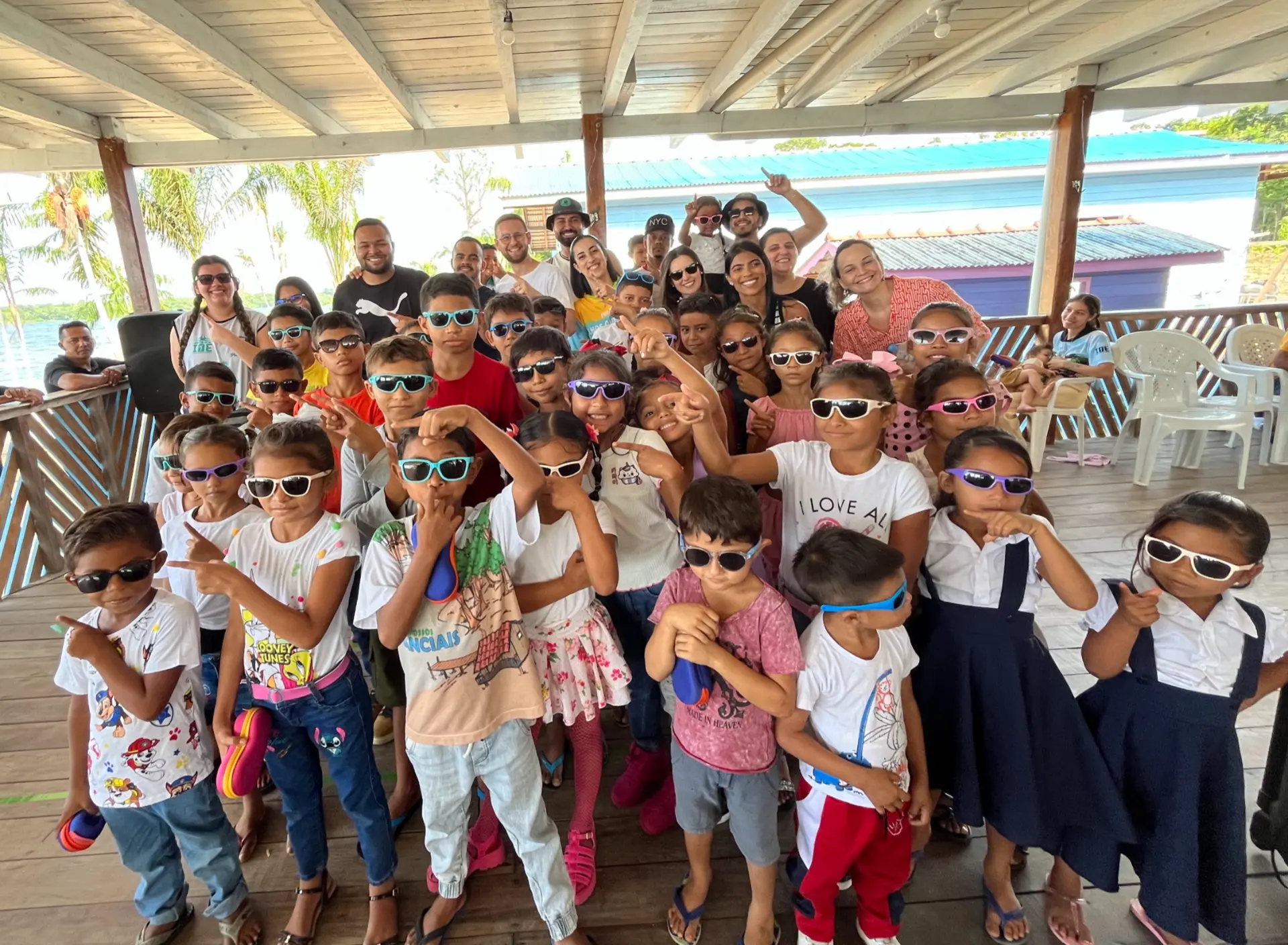 Grupo de cerca de 30 crianças com óculos de sol coloridos posa com voluntários da ação social no Marajó